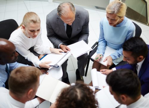 Circle of contemporary business people with documents having discussion of their reports at briefing