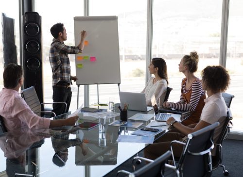 Rear view of a business manager using a flip chart board for explain his plan to his business colleagues in a modern office
